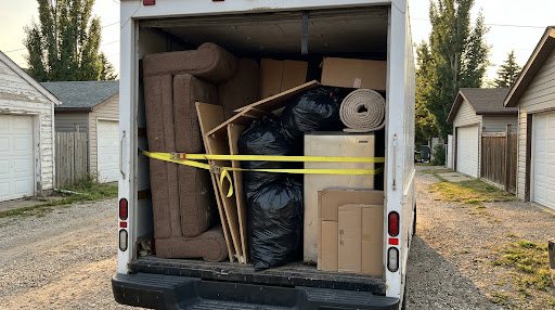 A cube van loaded with an old sofa, bagged waste, flattened cardboard and a rolled carpet, strapped before the haul